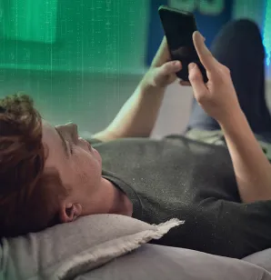 Un adolescent est couché et regarde son cellulaire.