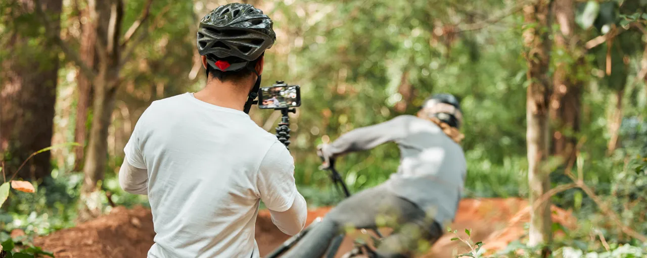 Deux personnes font du vélo. Une des personnes filme l’autre au moyen de son téléphone intelligent.