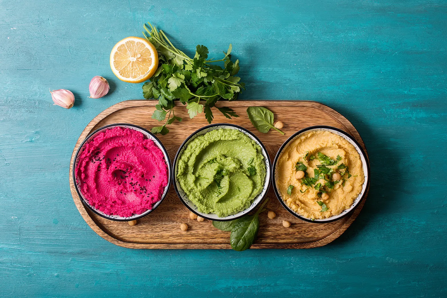 Il y a trois bols. Le premier contient de l’humus, le deuxième, de l’humus à l’avocat et le troisième, de l’humus aux betteraves. Les bols sont sur une planche de bois.